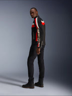 Un hombre vistiendo la chaqueta Alpinestars T-Dyno Air en negro, rojo brillante y crudo, chaqueta de moto textil de inspiración vintage con paneles de malla, marca llamativa en la manga, combinada con pantalones negros y botas para un look de motociclista moderno