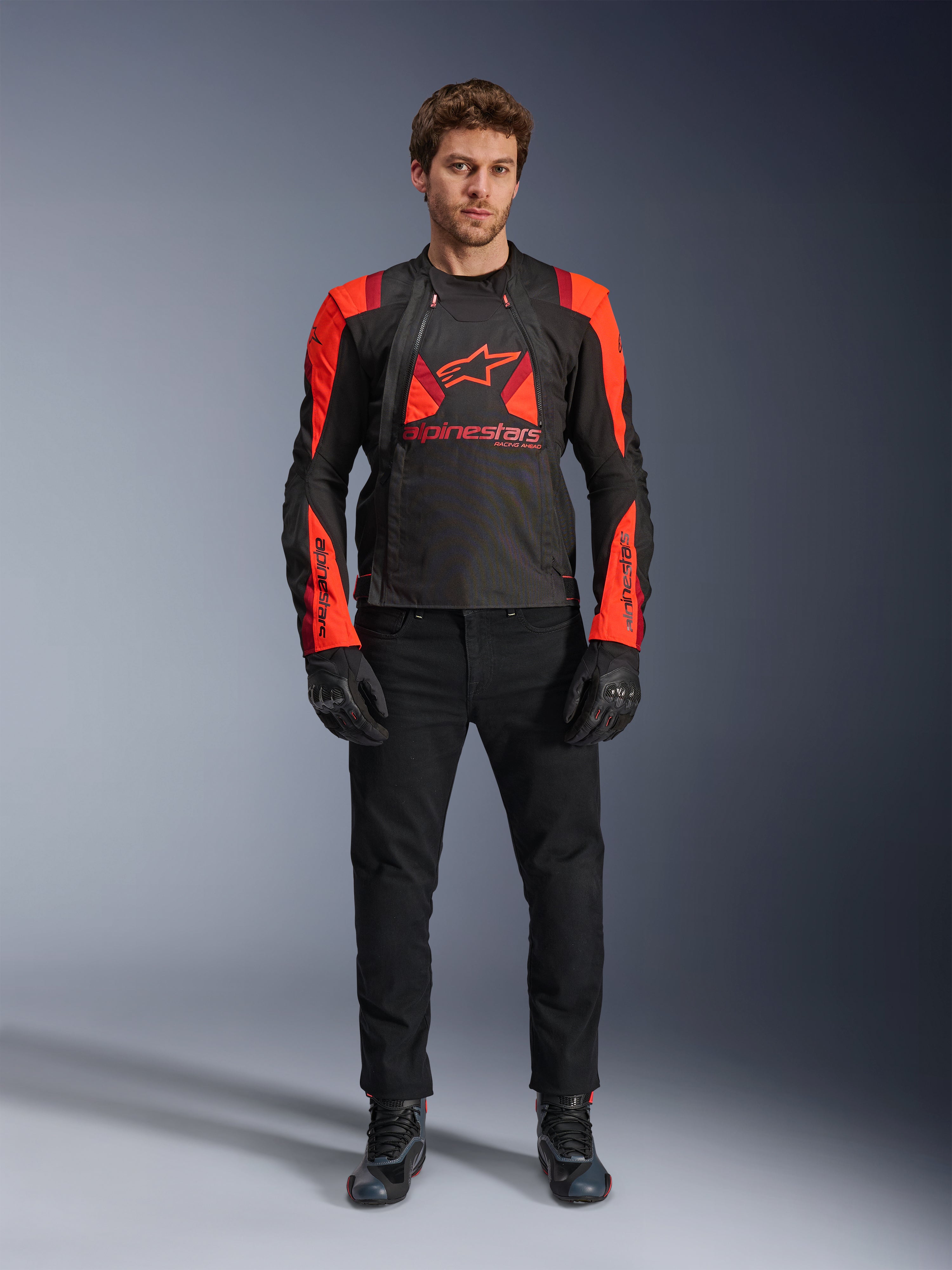 Chaqueta Alpinestars T-Stunt Air, negro, rojo fluo y rojo oscuro, usada por un modelo con vaqueros de moto negros y guantes, diseño modular 2 en 1 con paneles de malla prominentes para flujo de aire, equipamiento de moto de corte deportivo para carretera