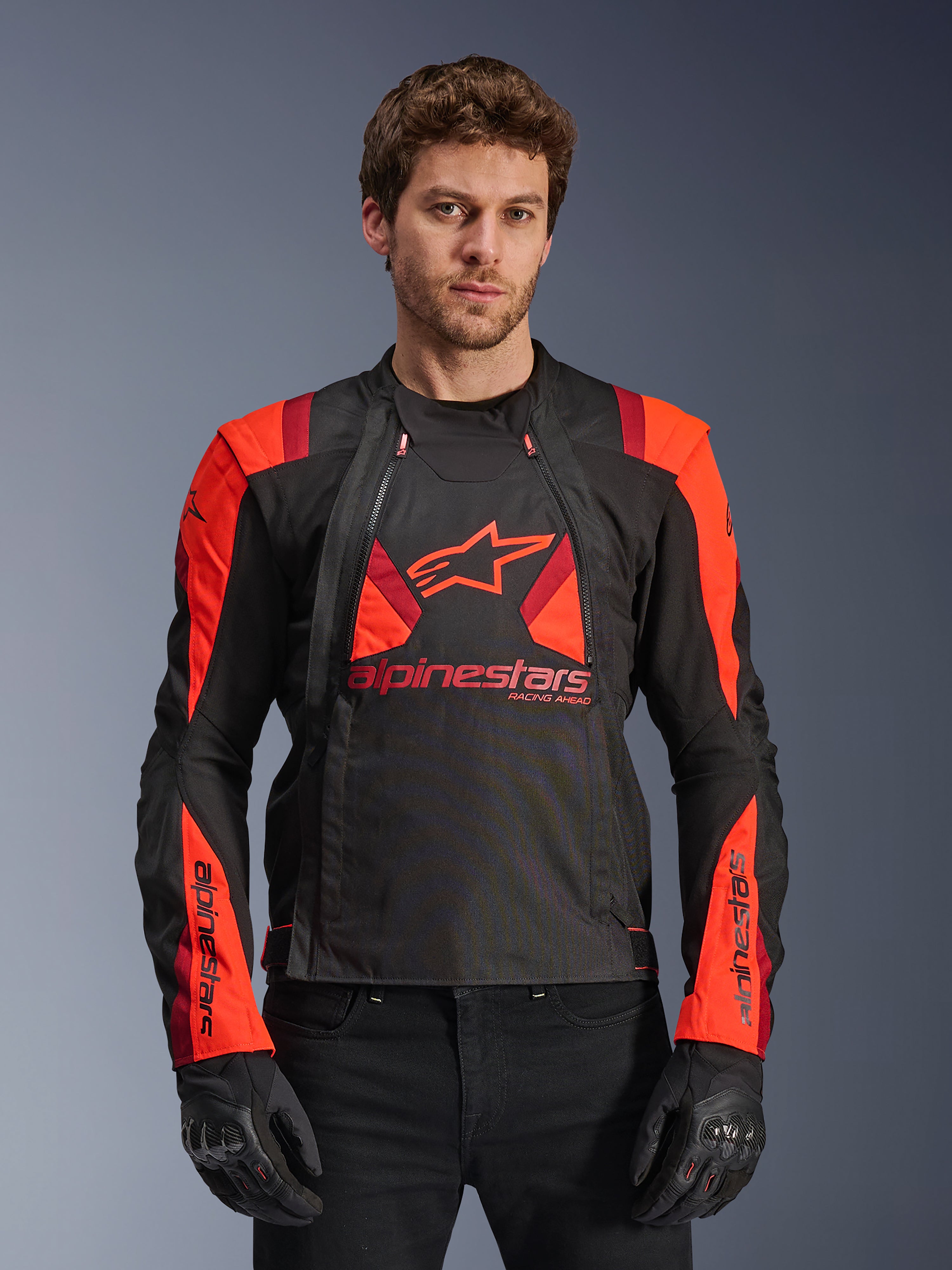 Alpinestars T-Stunt Air Jacket, chaqueta de moto textil, negro, rojo fluo y rojo oscuro, con un gran logo de estrella y paneles de malla para el flujo de aire, usada por un modelo con guantes negros