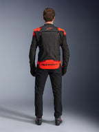 Chaqueta Alpinestars T-Stunt Air, negra con detalles en rojo flúor y rojo oscuro, vista posterior en modelo, combinada con pantalones y botas de moto negros, con un llamativo logotipo de Alpinestars en el panel inferior de la espalda, diseño modular con construcción de malla para ventilación.