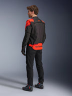 Hombre con la chaqueta Alpinestars T-Stunt Air vista desde atrás, negro, rojo fluo y rojo oscuro, chaqueta de moto textil con paneles de malla y diseño de corte deportivo, con un llamativo logotipo de Alpinestars en la parte baja de la espalda, combinada con pantalones negros y botas de motociclista