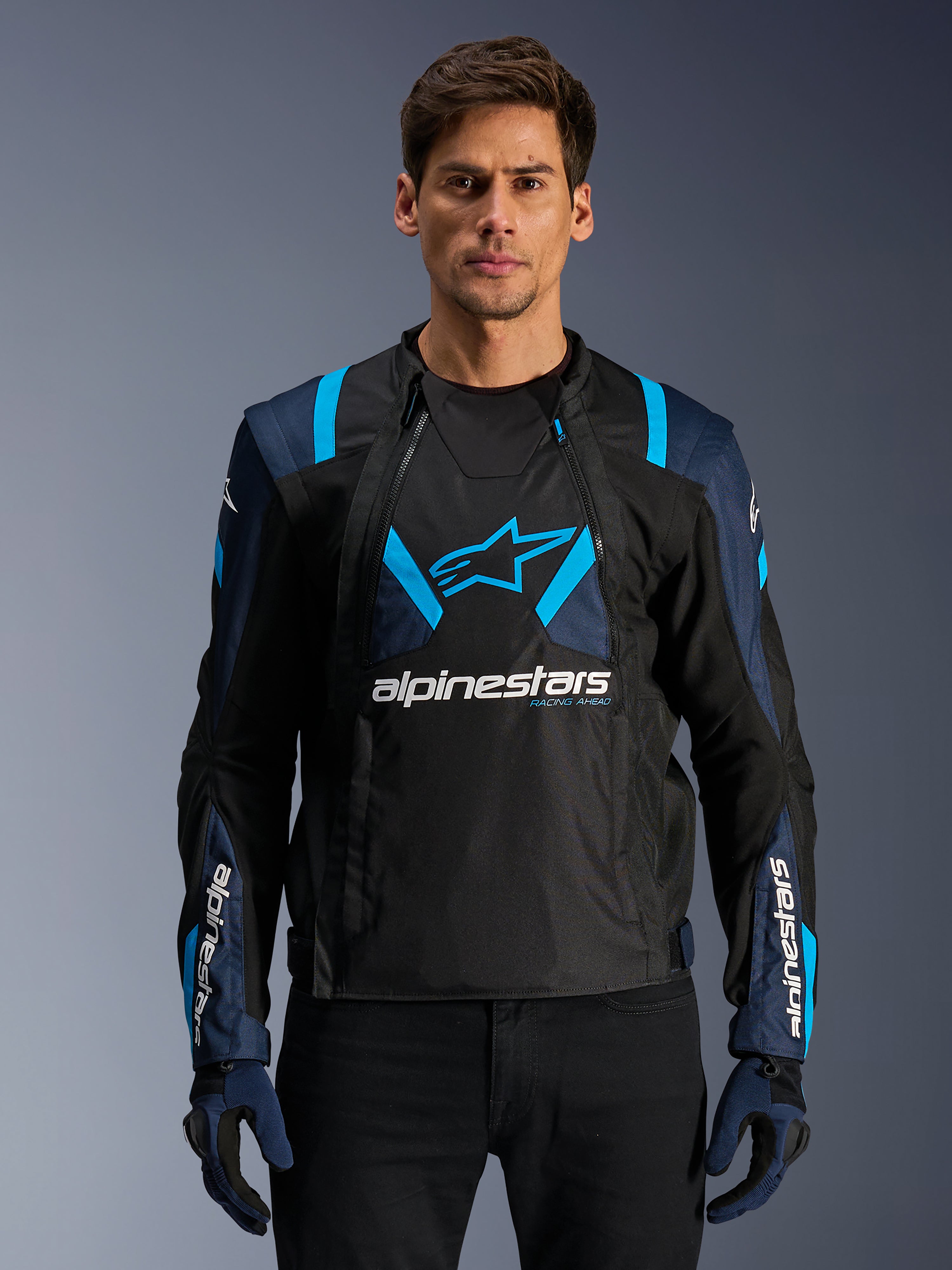 Alpinestars T-Stunt Air Jacket, chaqueta de malla para moto, negra y azul, usada por un modelo con pantalones y guantes negros, con un diseño modular 2 en 1, paneles de malla técnica transpirable, logo de estrella en el pecho y marca Alpinestars en las mangas
