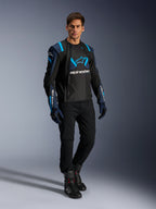 Modelo masculino con la chaqueta Alpinestars T-Stunt Air en negro, azul oscuro y azul Blithe, con paneles de malla para ventilación, combinada con pantalones negros y guantes de conducción; chaqueta de moto de corte deportivo para carretera en verano.
