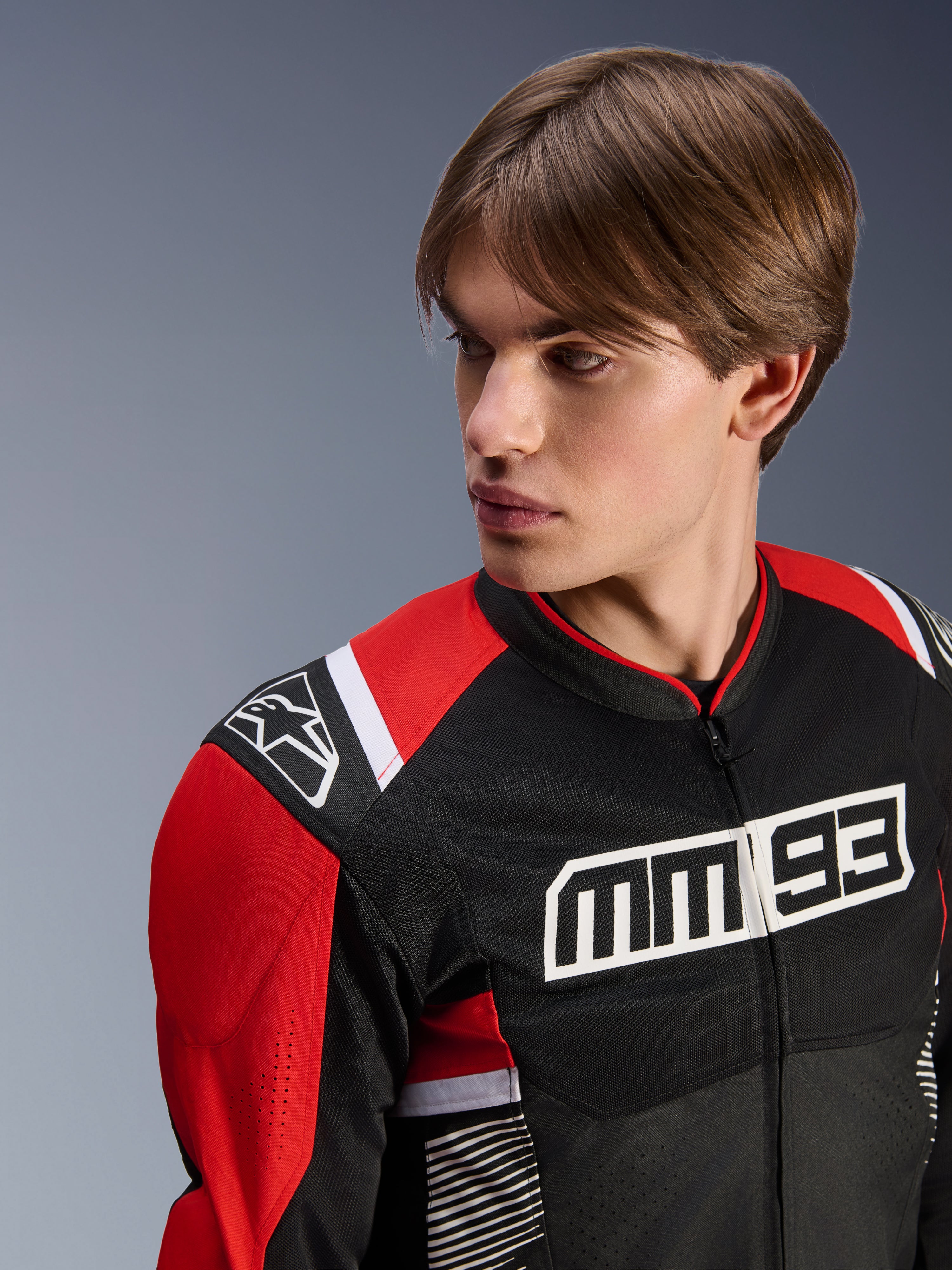 Modelo masculino luciendo la chaqueta Alpinestars MM93 T-SPS Air V2, chaqueta textil para moto, en negro, rojo brillante y blanco, con el llamativo logotipo MM 93 en el pecho y el logo de la estrella en el hombro, construcción de malla para el flujo de aire, equipamiento de conducción deportivo