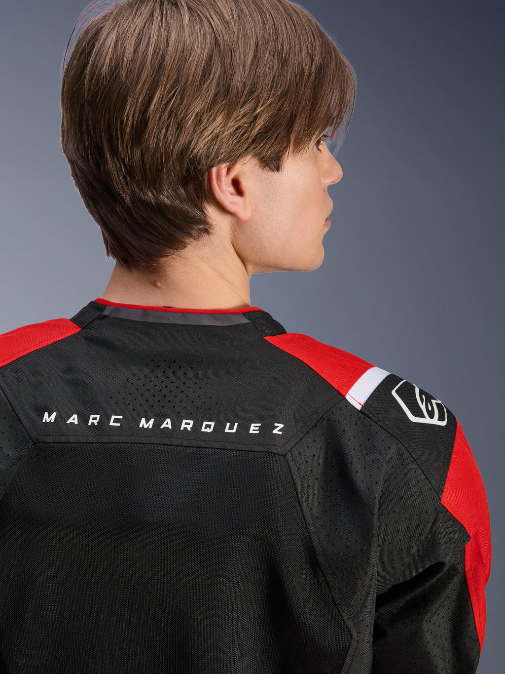 Chaqueta Alpinestars MM93 T-SPS Air V2, vista posterior de la parte superior de la espalda y los hombros, negro con detalles en rojo brillante y blanco, texto 'MARC MARQUEZ' en el canesú, con paneles de malla técnica y logotipo en el hombro, ropa de moto deportiva urbana