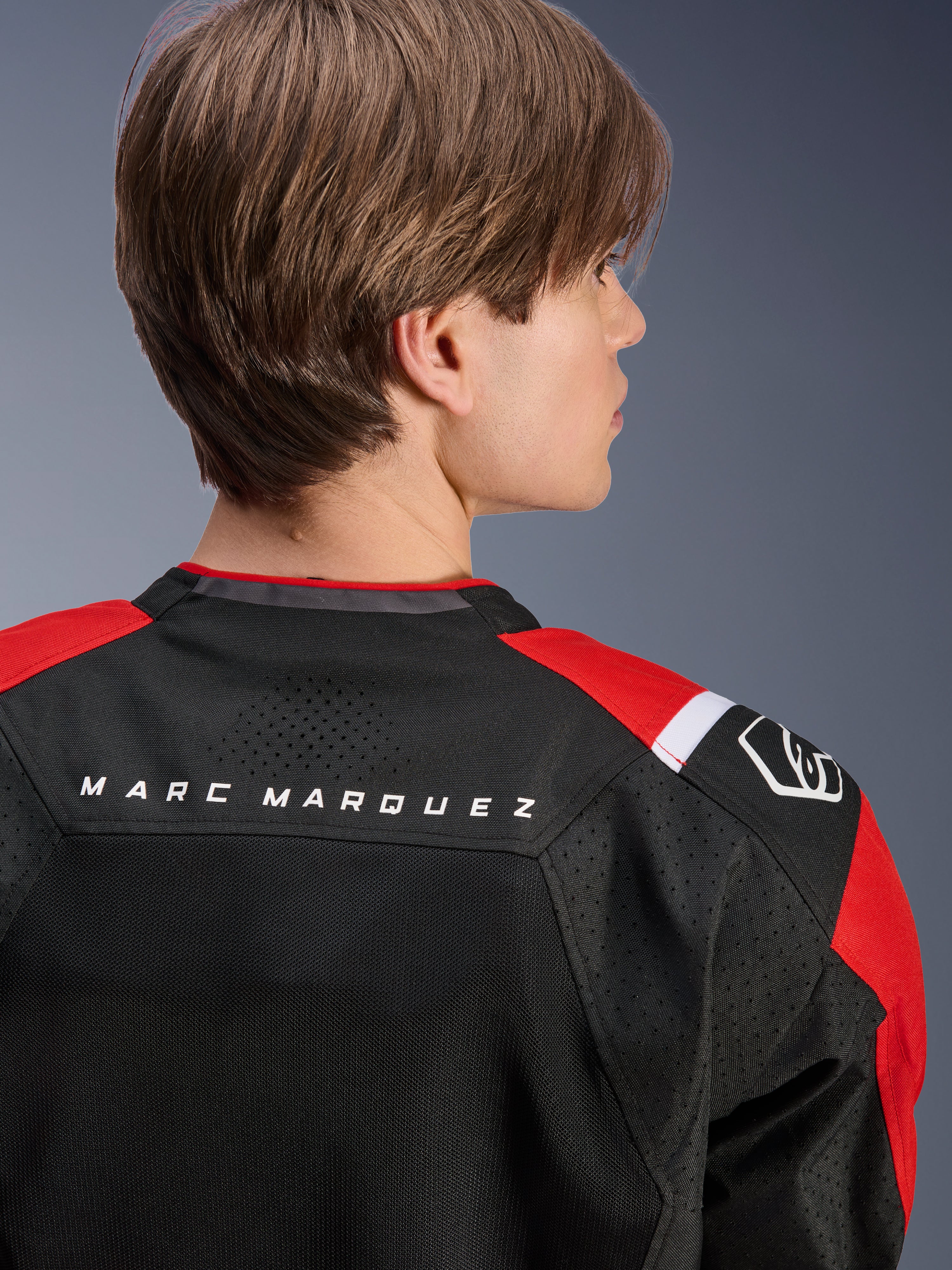 Chaqueta Alpinestars MM93 T-SPS Air V2, vista posterior de la parte superior de la espalda y los hombros, negro con detalles en rojo brillante y blanco, texto 'MARC MARQUEZ' en el canesú, con paneles de malla técnica y logotipo en el hombro, ropa de moto deportiva urbana