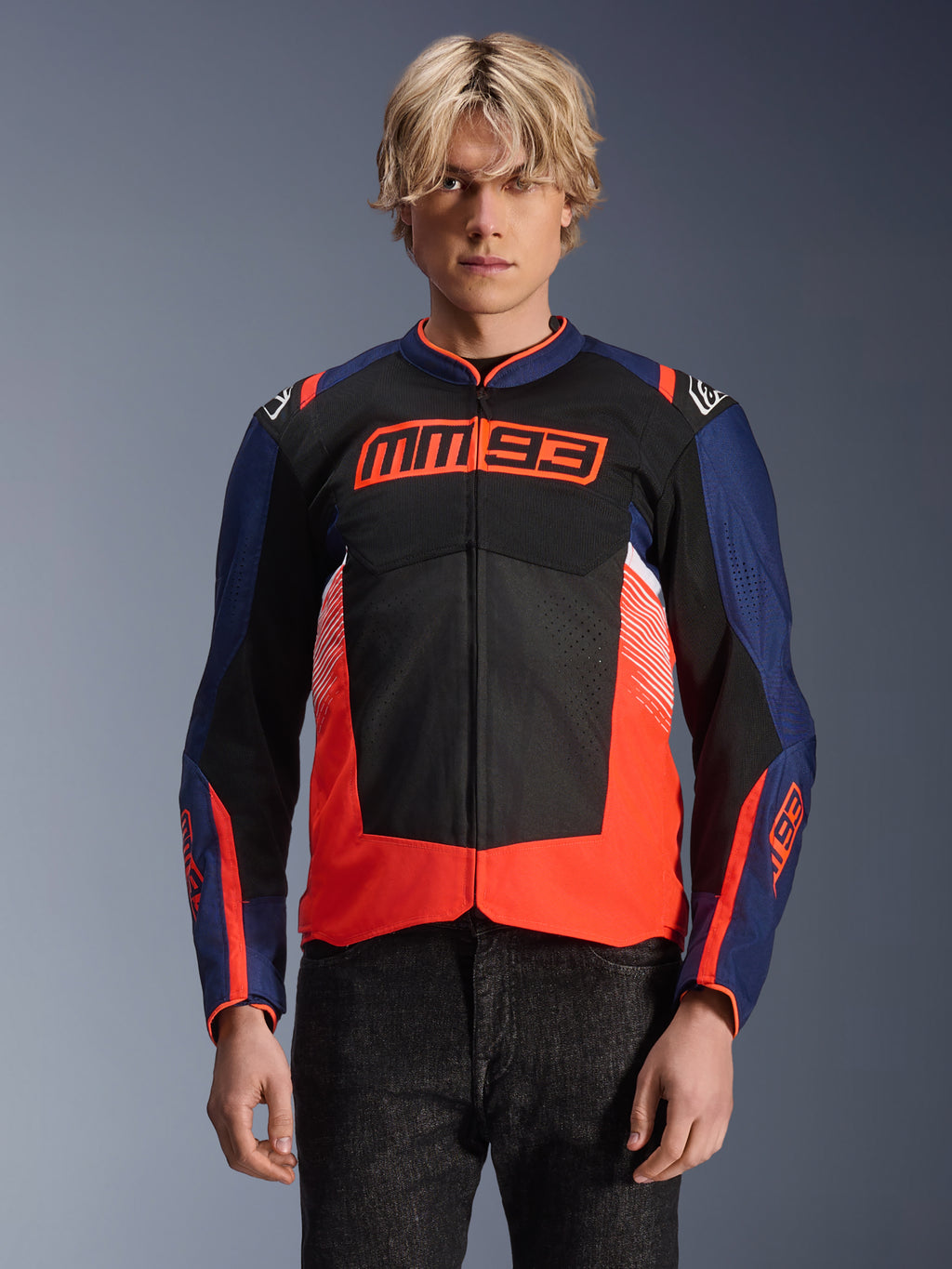 Chaqueta Alpinestars MM93 T-SPS Air V2, chaqueta textil de moto, azul marino, negro y rojo fluorescente, vestida por una persona, con el logotipo MM93 destacado en el pecho, paneles de malla para ventilación y diseño moderno de bloques de color