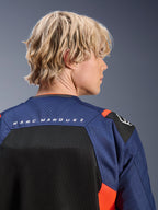 Chaqueta Alpinestars MM93 T-SPS Air V2, azul marino y negro con detalles en rojo flúor, primer plano de la parte superior de la espalda con la marca 'MARC MARQUEZ', paneles de malla transpirable y construcción textil perforada, usada por un modelo rubio.