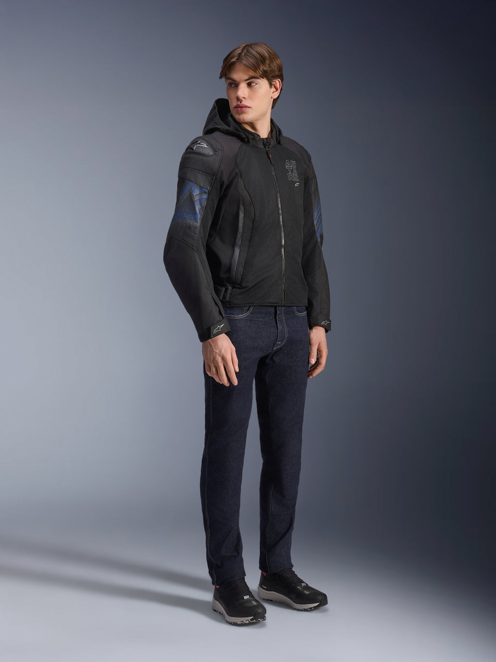 Chaqueta Alpinestars Zaca Air Venom WP, chaqueta de moto textil en color negro y azul eléctrico, usada por un modelo con vaqueros oscuros y zapatillas negras, con capucha desmontable, paneles de ventilación de malla y deslizadores de hombro DFS Lite, equipamiento deportivo para todo tipo de clima