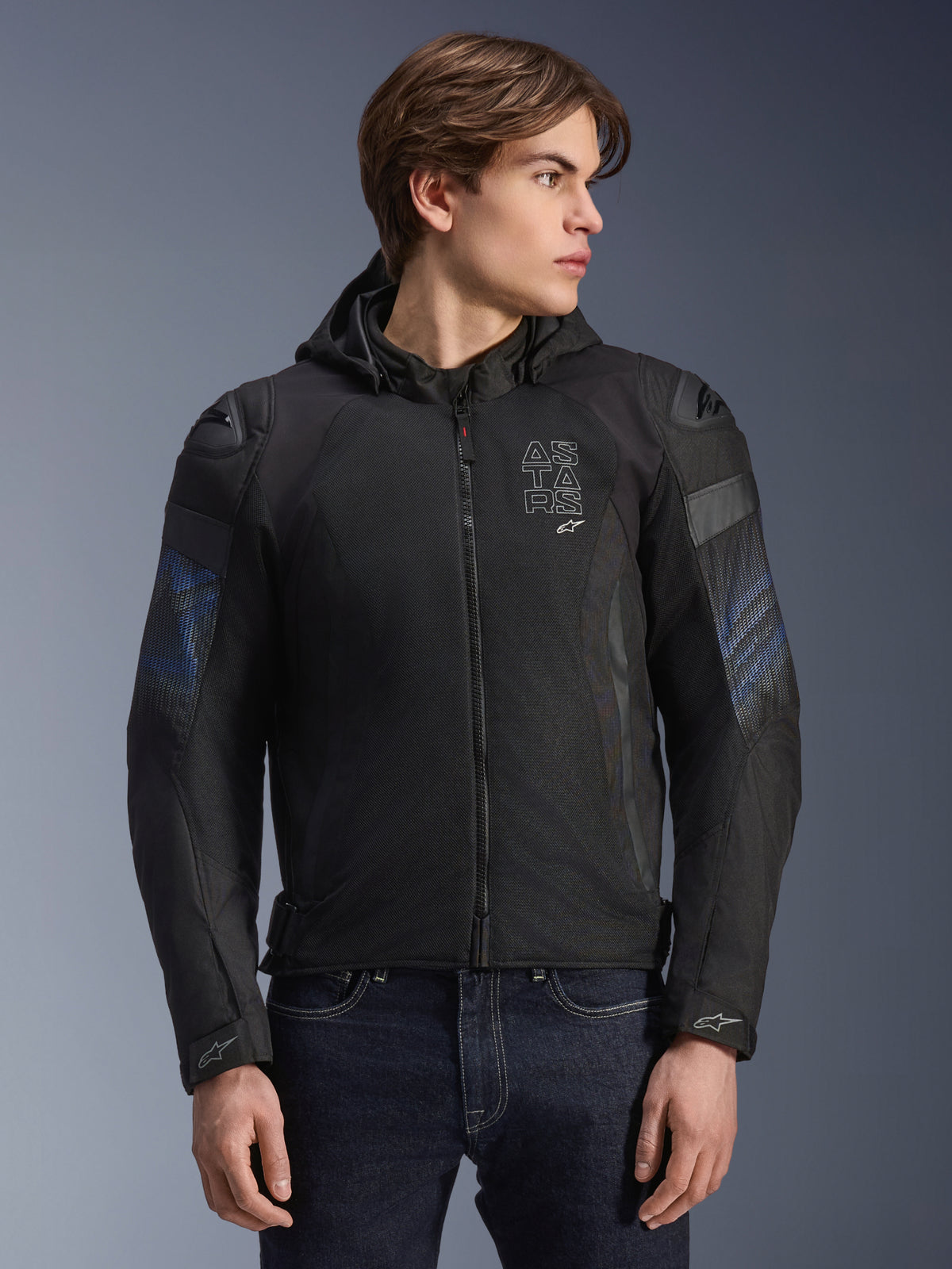 Chaqueta Alpinestars Zaca Air Venom WP, negra y azul eléctrico, chaqueta de moto textil con capucha desmontable y paneles de malla 3D para ventilación, incluye deslizadores de hombro DFS Lite y logotipo ASTARS en el pecho, usada por un modelo masculino, equipamiento de conducción urbana de estilo deportivo