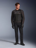Modelo masculino con la chaqueta de moto Alpinestars SMX Air en color Black Anthracite, con paneles de malla ventilada y logo gris en el pecho, combinada con pantalones negros y guantes protectores, en un entorno de estudio con fondo degradado
