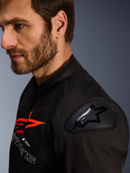 Chaqueta Alpinestars SMX Air, negra y roja, detalle en primer plano del protector de hombro DFS Lite con logo de estrella, usada por un hombre con barba, chaqueta textil de motociclismo para carreras y deportiva.