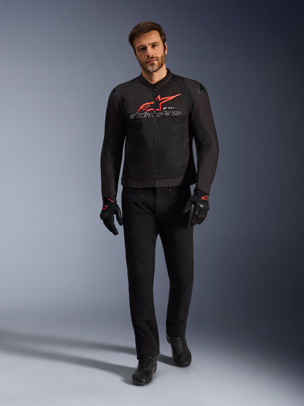 Chaqueta Alpinestars SMX Air, negro, rojo brillante y blanco, chaqueta de moto deportiva usada con pantalones y guantes negros, con paneles de malla técnica y un llamativo logotipo rojo de Alpinestars en el pecho, conjunto de conducción urbana de alto rendimiento