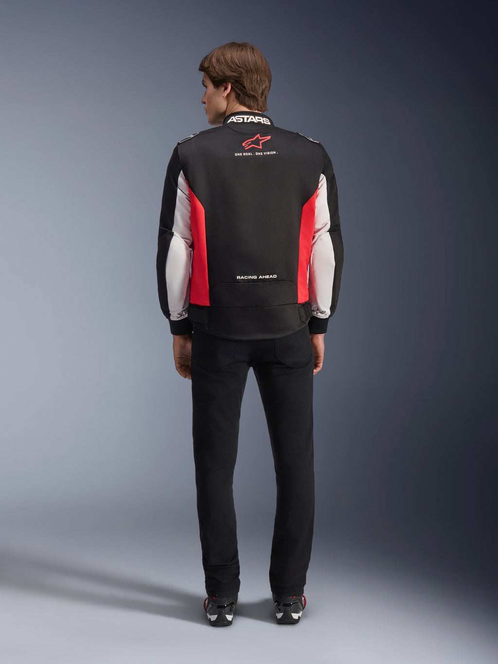 Alpinestars Monza Sport Jacket, Black Bright Red and White textile motorcycle jacket, rear view shown on a model, featuring red star logo and 'ASTARS' collar branding with slogans, worn with black pants and riding boots.
