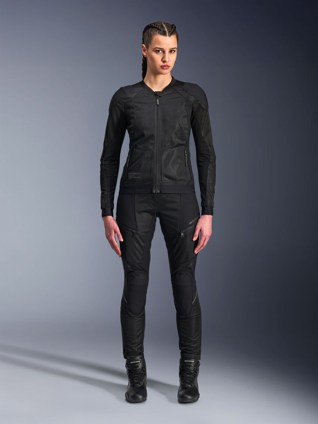 Chaqueta Alpinestars Stella Troop-Air, chaqueta de moto para mujer, negra, construcción de malla técnica 2D con diseño minimalista, usada con pantalones de conducción y botas negras, estilo de motociclismo urbano contemporáneo.