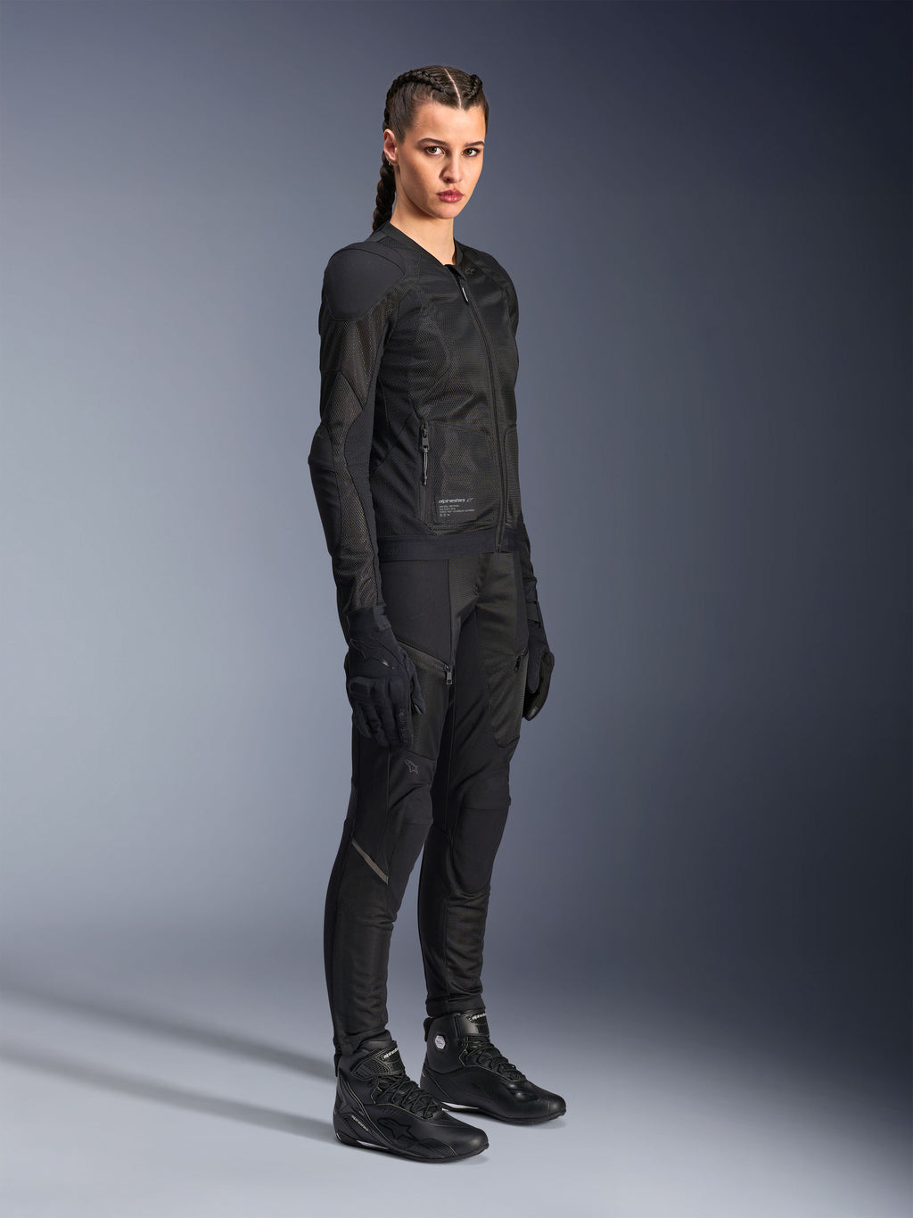 Mujer piloto vistiendo la chaqueta Alpinestars Stella Troop-Air en color negro, con construcción técnica de malla 2D, combinada con pantalones, guantes y botas de moto negros a juego, diseñada para conducción urbana