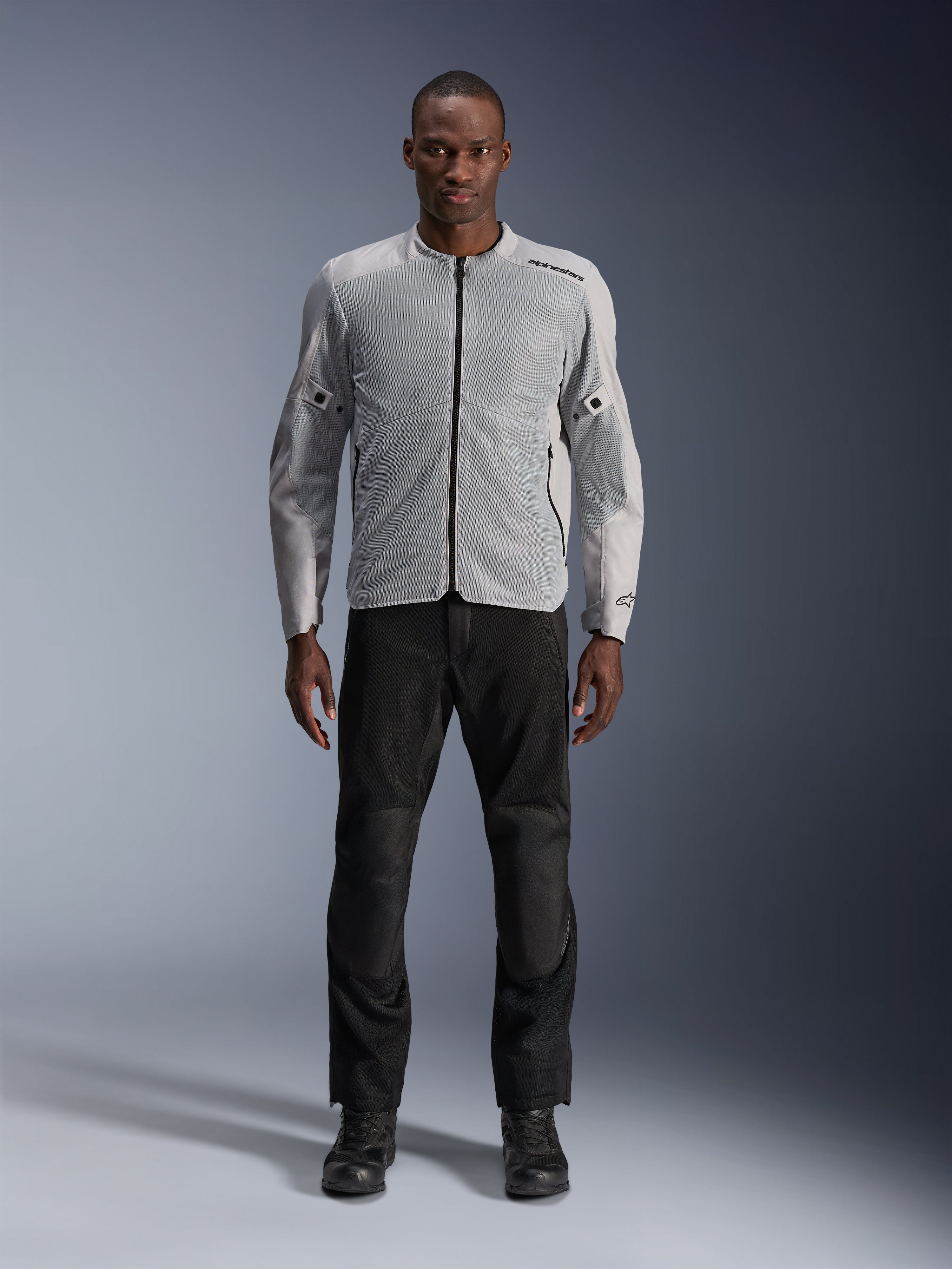Alpinestars C-1 Air Jacket en Silver, chaqueta de moto textil urbana para hombre con paneles de malla ventilada, usada por un modelo con pantalones de moto negros y botas negras, estilo contemporáneo para trayectos urbanos