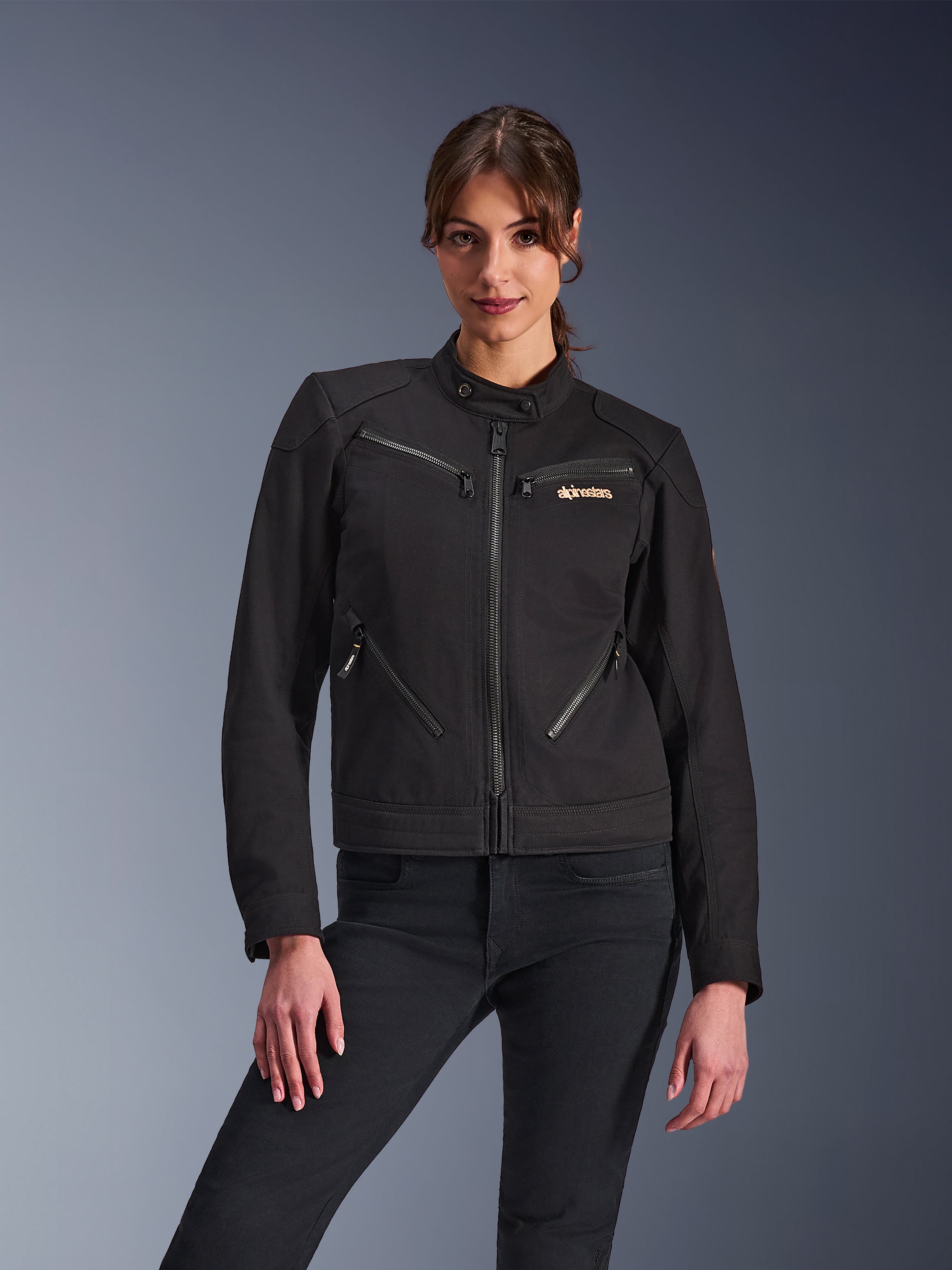 Chaqueta Alpinestars Stella Grace para mujer, chaqueta de moto urbana, negra, vista frontal, con múltiples bolsillos con cremallera y cuello con botón a presión, combinada con vaqueros negros, equipamiento de protección para mujer de estilo urbano moderno