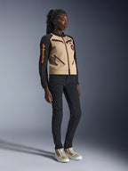 Modelo con la Chaqueta Alpinestars Stella Grace en Aluminum Black, con torso de color canela y mangas negras con detalles de cremalleras rojas, combinada con pantalones negros ajustados y zapatillas crema, ropa de motociclismo urbana contemporánea para mujer