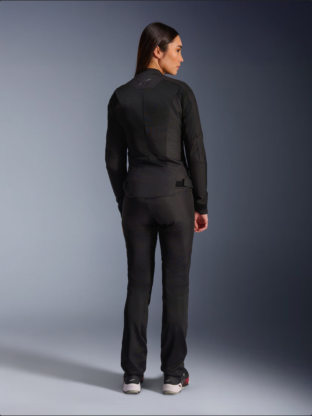 Chaqueta Alpinestars Stella C-1 Air, chaqueta de moto textil para mujer, negra, vista trasera mostrando la construcción de malla y un sutil logotipo en la parte superior de la espalda, combinada con pantalones de conducción negros a juego, estilo urbano contemporáneo