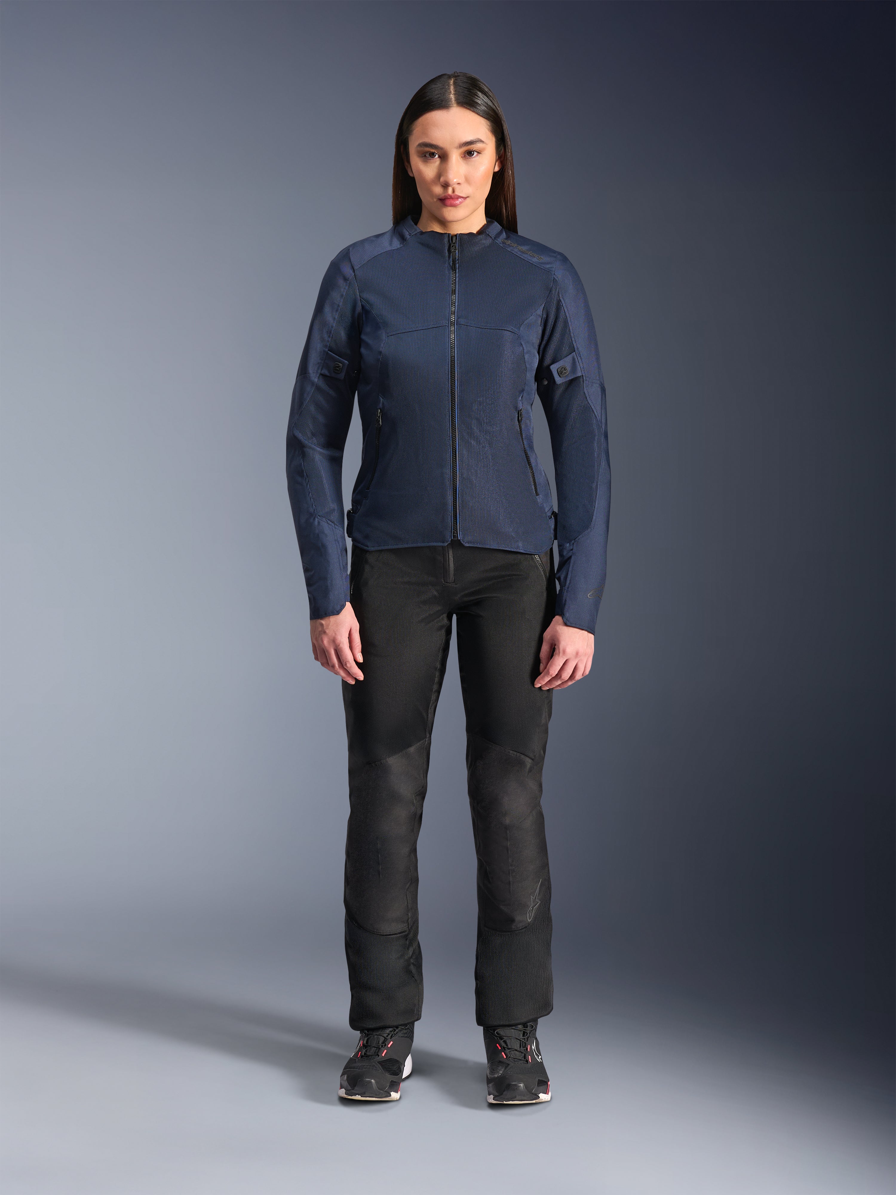 Modelo femenina luciendo la chaqueta Alpinestars Stella C-1 Air en color azul, chaqueta urbana para moto con paneles de malla técnica, combinada con pantalones de motociclista negros y zapatillas negras, vista frontal de estudio