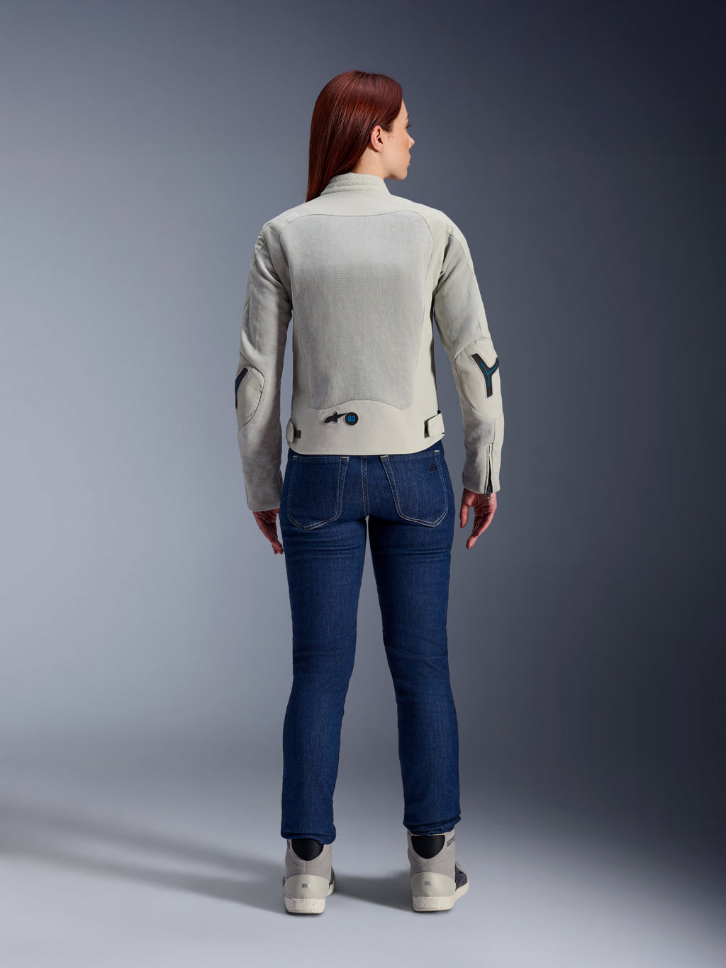 Alpinestars Woman Stella Circal-1 Air Jacket in Metal Gray and Methyl Blue, rear view, featuring large mesh airflow panels on the back and arms, worn with dark blue denim jeans and gray riding shoes for a modern urban motorcycle look.