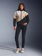 Chaqueta Alpinestars Stella Moshell para mujer, chaqueta urbana de motociclismo con un diseño asimétrico de bloques de color en negro, arena y blanco roto, combinada con pantalones negros de corte ajustado y zapatillas altas de color arena, estética streetwear moderna para motoristas.