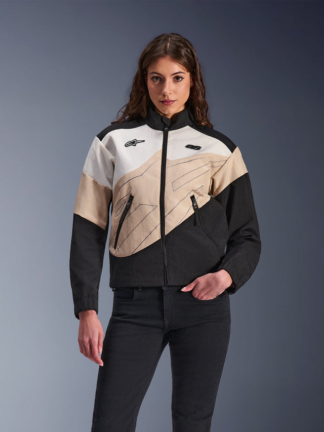 Chaqueta Alpinestars Stella Moshell, chaqueta de moto urbana para mujer, diseño de bloques de color asimétricos en negro, arena y blanco roto, con cremallera frontal y bolsillos para las manos con cremallera, combinada con pantalones negros para un look urbano contemporáneo.