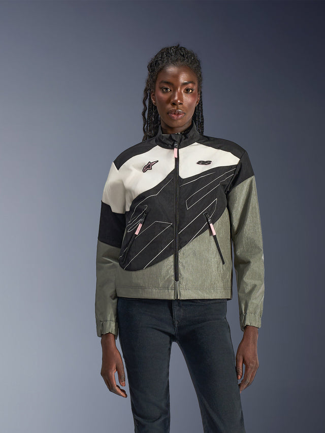 Mujer con la Chaqueta Alpinestars Stella Moshell, chaqueta urbana para motocicleta en negro, gris, blanco roto y rosa, diseño asimétrico con gráficos técnicos, tiradores de cremallera rosas y logotipos de Alpinestars, estilo streetwear contemporáneo para motociclistas urbanas.