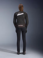 Chaqueta Alpinestars Stella T-GP Plus R V4 Airflow, negra y blanca, vista trasera que muestra paneles de ventilación de malla extensiva y la marca Alpinestars, usada por una motociclista con pantalones de moto negros de ajuste ceñido y botas, equipamiento textil deportivo para mujer