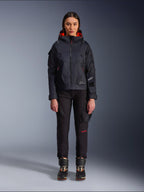 Pantalones Alpinestars Actea para mujer, pantalones de moto negros con detalles de texto en rojo y bolsillos cargo, usados por una motorista con una chaqueta negra con capucha, ropa de moto urbana moderna