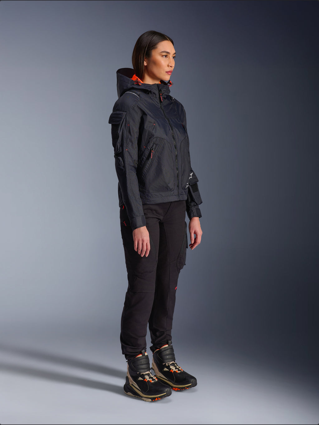 Pantalones Alpinestars Actea para mujer en negro, corte regular con bolsillos cargo, combinados con una chaqueta Molly Air negra con detalles naranjas y calzado de conducción de caña alta, ropa de moto urbana contemporánea para mujer