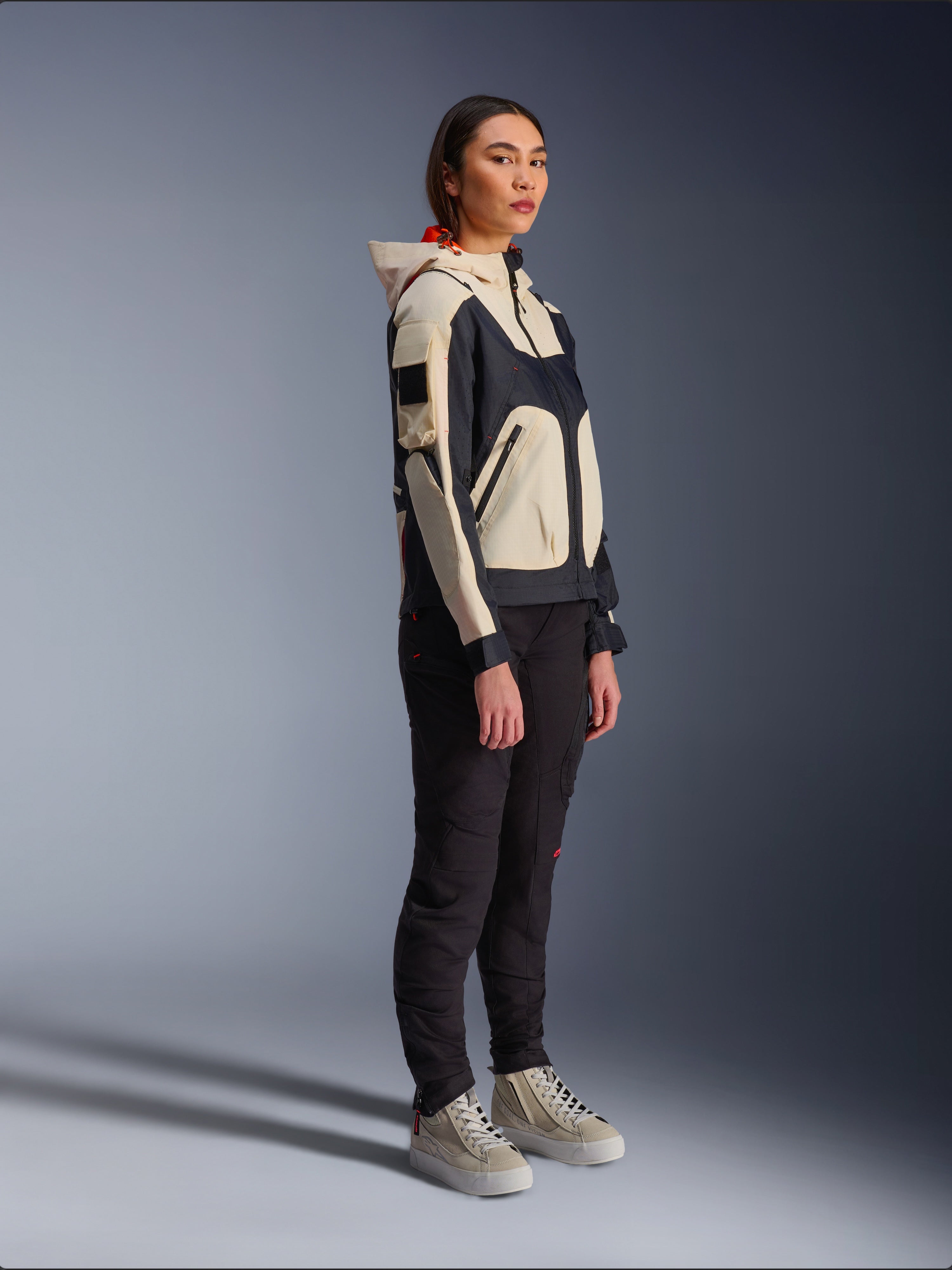 Alpinestars Molly Air Jacket in Black Almond, worn by a female rider with black pants and cream high-top sneakers, featuring a two-tone design with black and beige panels, integrated hood, and contemporary urban style.