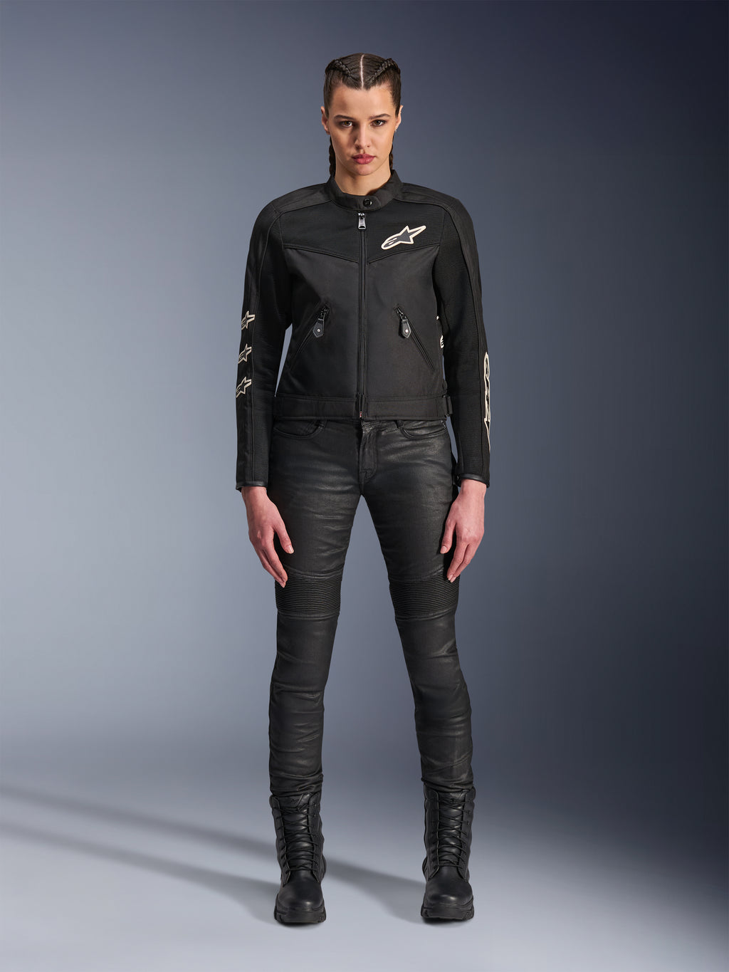 Modelo femenina luciendo la chaqueta Alpinestars Stella T-Dyno Air, chaqueta de moto para mujer en negro, con paneles de malla 3D y logotipos Astars blancos, combinada con pantalones de montar negros de corte ajustado y botas negras con cordones, estilo de equipamiento de conducción urbana.