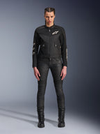Modelo femenina luciendo la chaqueta Alpinestars Stella T-Dyno Air, chaqueta de moto para mujer en negro, con paneles de malla 3D y logotipos Astars blancos, combinada con pantalones de montar negros de corte ajustado y botas negras con cordones, estilo de equipamiento de conducción urbana.