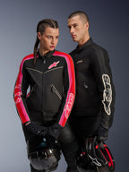 Chaqueta Alpinestars Stella T-Dyno Air para mujer en color negro, rojo brillante y fucsia, combinada con la chaqueta Dyno Air negra para hombre, ambos motociclistas sosteniendo cascos de moto, fotografía de estudio de equipamiento de motociclismo urbano contemporáneo