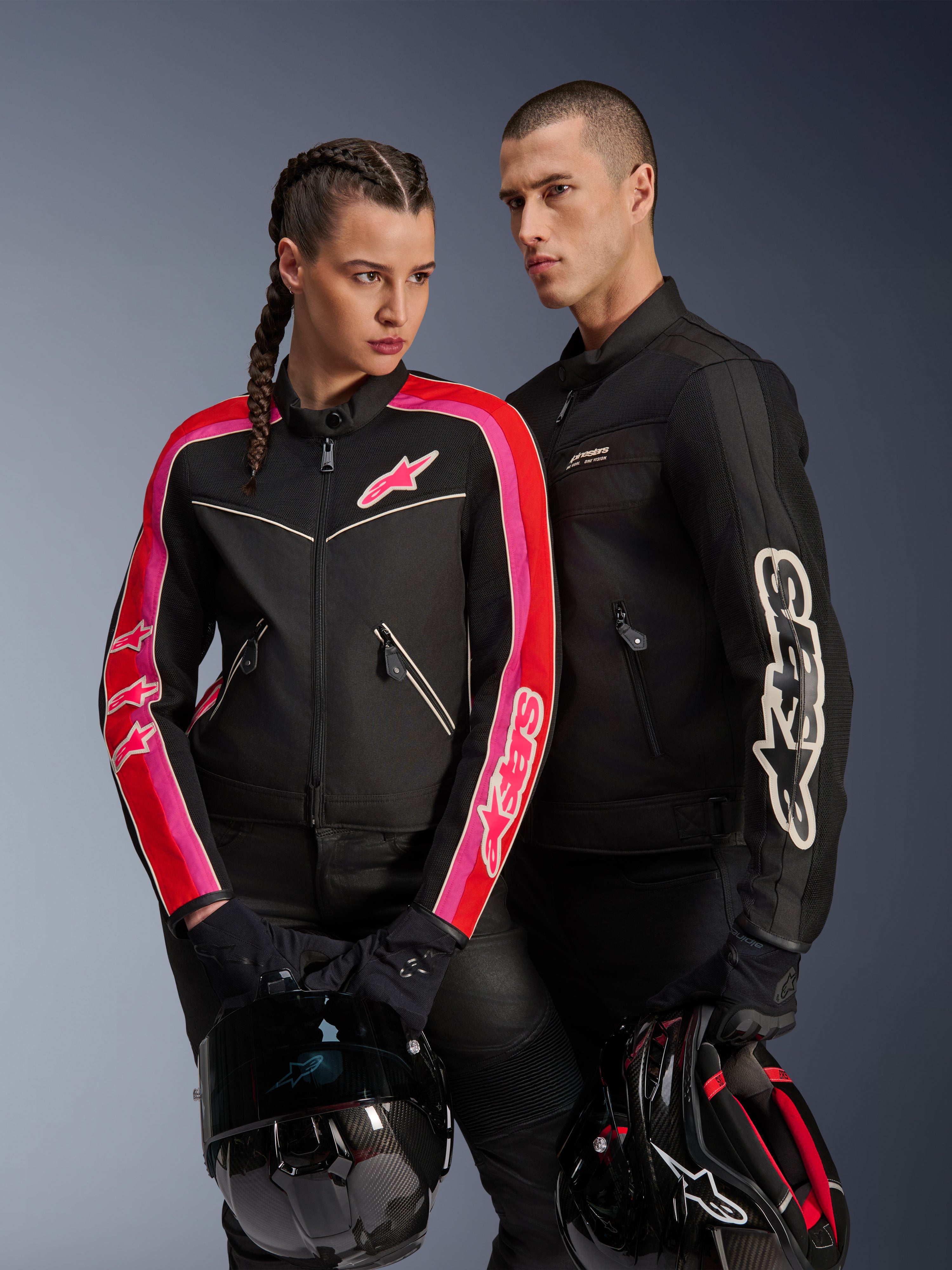 Chaqueta Alpinestars Stella T-Dyno Air para mujer en color negro, rojo brillante y fucsia, combinada con la chaqueta Dyno Air negra para hombre, ambos motociclistas sosteniendo cascos de moto, fotografía de estudio de equipamiento de motociclismo urbano contemporáneo