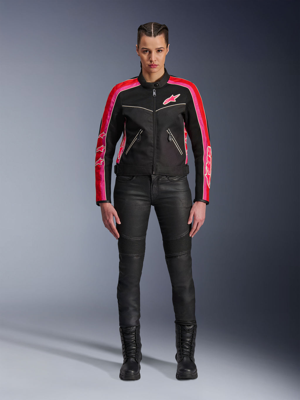 Mujer motociclista con la chaqueta Alpinestars Stella T-Dyno Air, negra con detalles en rojo brillante y fucsia, combinada con pantalones de moto negros y botas con cordones, con paneles de malla 3D, ajuste entallado y logotipos de estrellas rosas, conjunto de equipamiento para conducción urbana