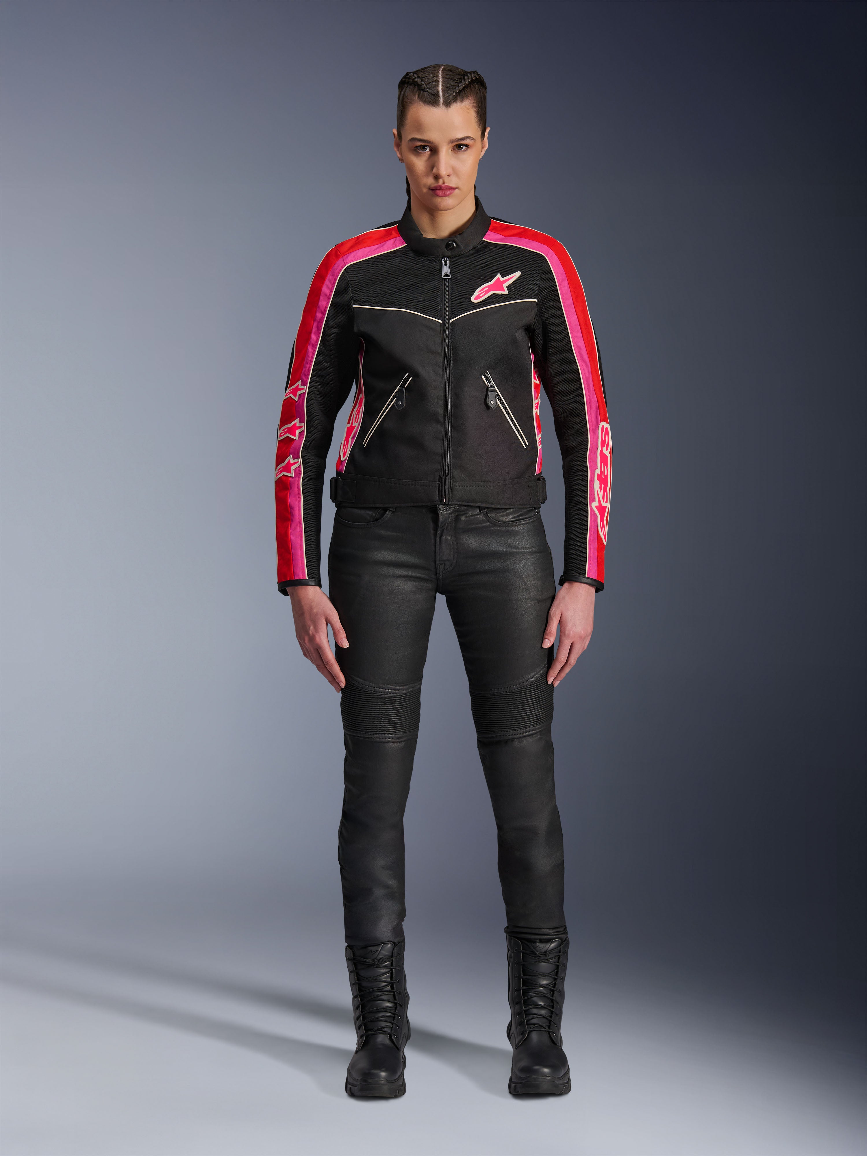 Mujer motociclista con la chaqueta Alpinestars Stella T-Dyno Air, negra con detalles en rojo brillante y fucsia, combinada con pantalones de moto negros y botas con cordones, con paneles de malla 3D, ajuste entallado y logotipos de estrellas rosas, conjunto de equipamiento para conducción urbana