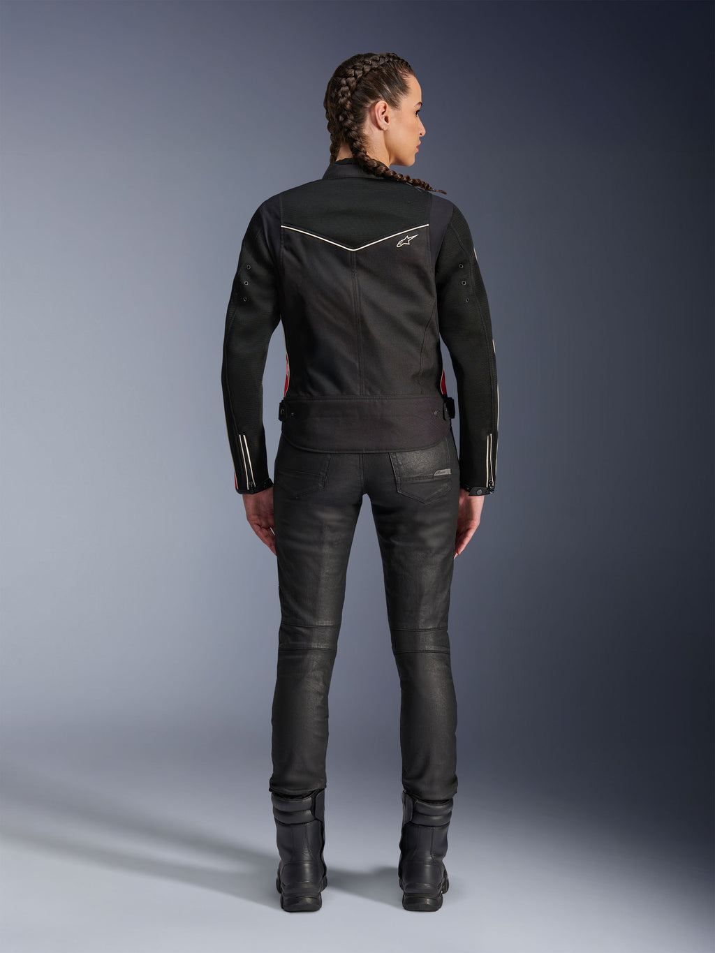Chaqueta Alpinestars Stella T-Dyno Air, vista trasera, chaqueta de moto negra para mujer con ribetes blancos y un pequeño logotipo de estrella, usada con pantalones técnicos negros y botas de motorista, ajuste elegante de motociclista para conducción urbana