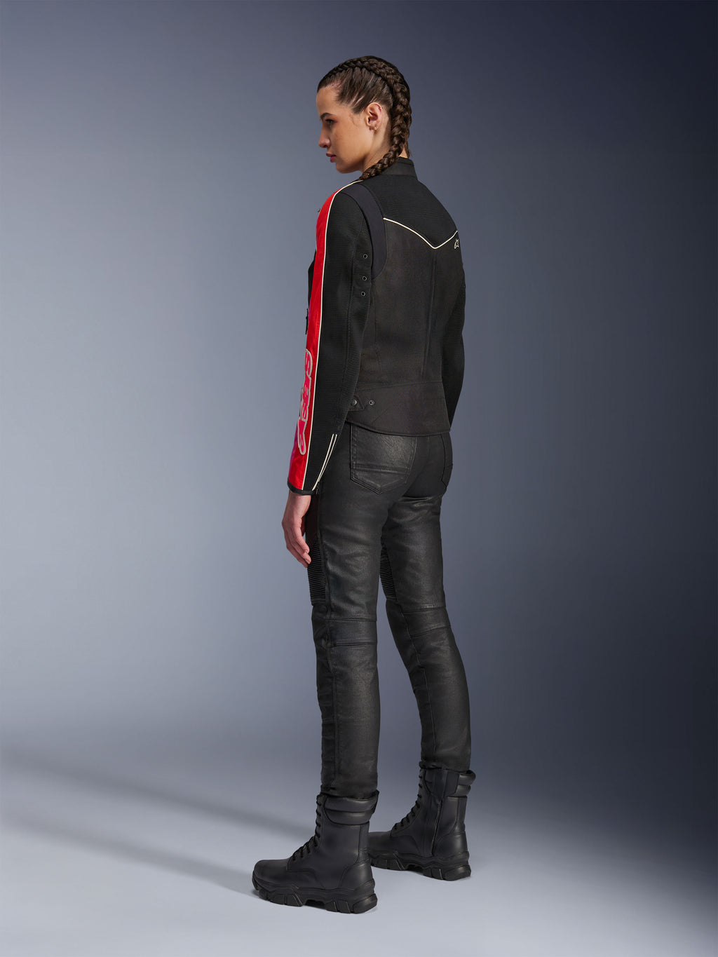 Mujer con la chaqueta Alpinestars Stella T-Dyno Air en color Negro Rojo Brillante Fucsia, combinada con pantalones de motociclista negros y botas negras, vista de perfil que resalta los gráficos rojos y fucsia de las mangas y el ajuste de motociclista entallado.