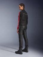 Mujer con la chaqueta Alpinestars Stella T-Dyno Air en color Negro Rojo Brillante Fucsia, combinada con pantalones de motociclista negros y botas negras, vista de perfil que resalta los gráficos rojos y fucsia de las mangas y el ajuste de motociclista entallado.
