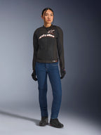 Piloto femenina con la chaqueta Alpinestars Stella SMX Air, negra con logotipos en blanco y rojo flúor, combinada con pantalones vaqueros azules y guantes negros, chaqueta textil deportiva ventilada para conducción en carretera