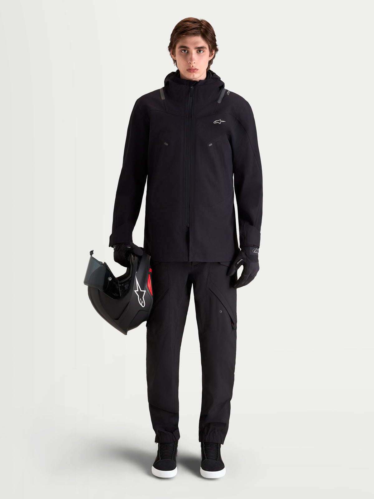 Alpinestars Juggernaut V 2 Drystar Pantalones, pantalones de moto urbanos contemporáneos para hombre, de color negro, vista frontal completa en un modelo que lleva chaqueta y casco a juego, con construcción textil impermeable