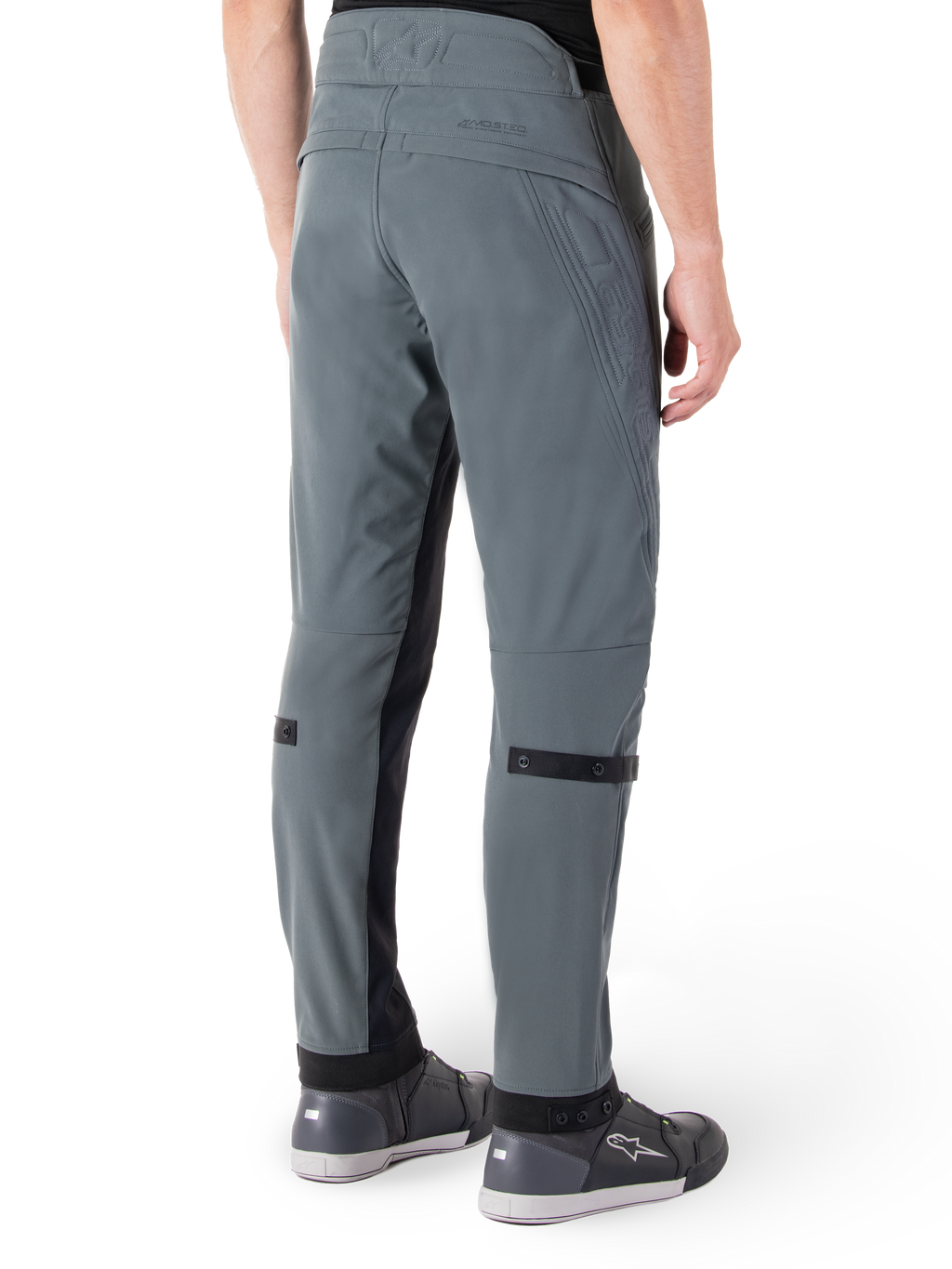 Pantalones Alpinestars Alden, Gris Urbano, vista lateral trasera, pantalones técnicos de conducción inspirados en el estilo urbano con detalles acolchados en la cintura y correas negras en la pantorrilla, combinados con calzado de conducción gris, equipamiento de motociclismo urbano moderno