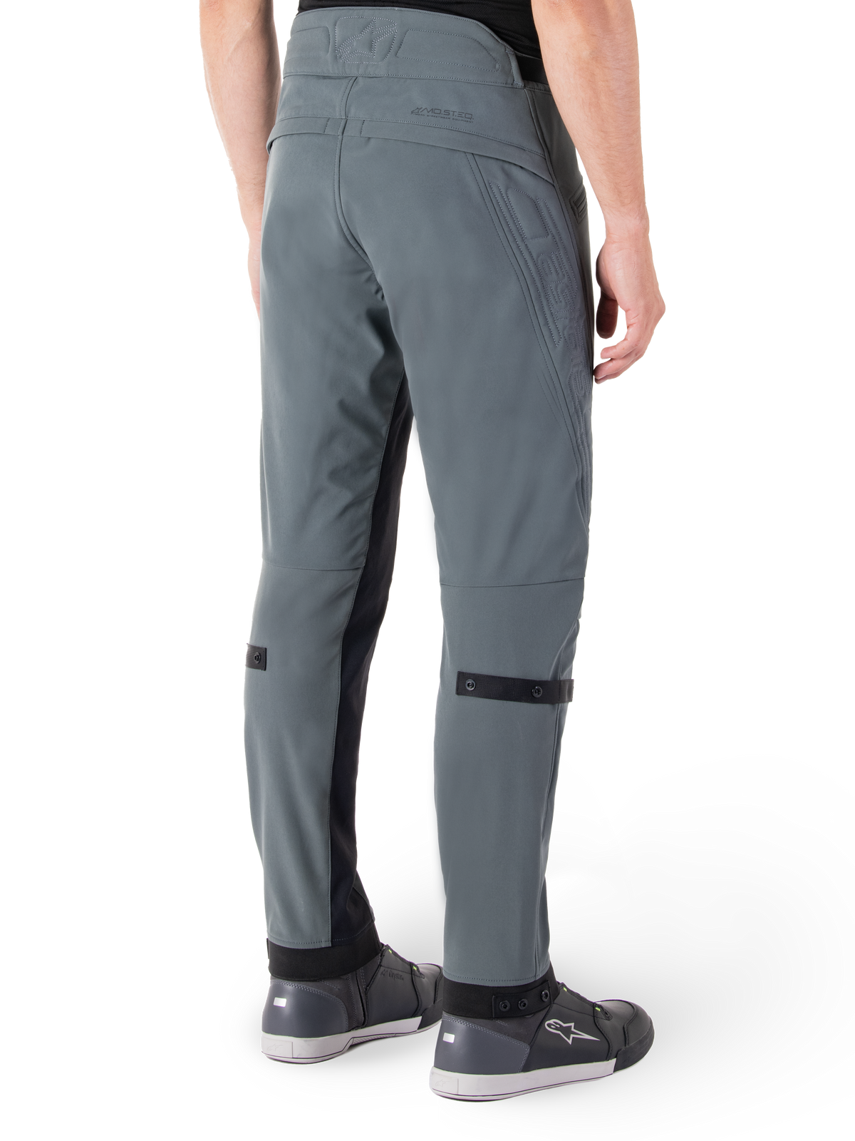 Pantalones Alpinestars Alden, Gris Urbano, vista lateral trasera, pantalones técnicos de conducción inspirados en el estilo urbano con detalles acolchados en la cintura y correas negras en la pantorrilla, combinados con calzado de conducción gris, equipamiento de motociclismo urbano moderno