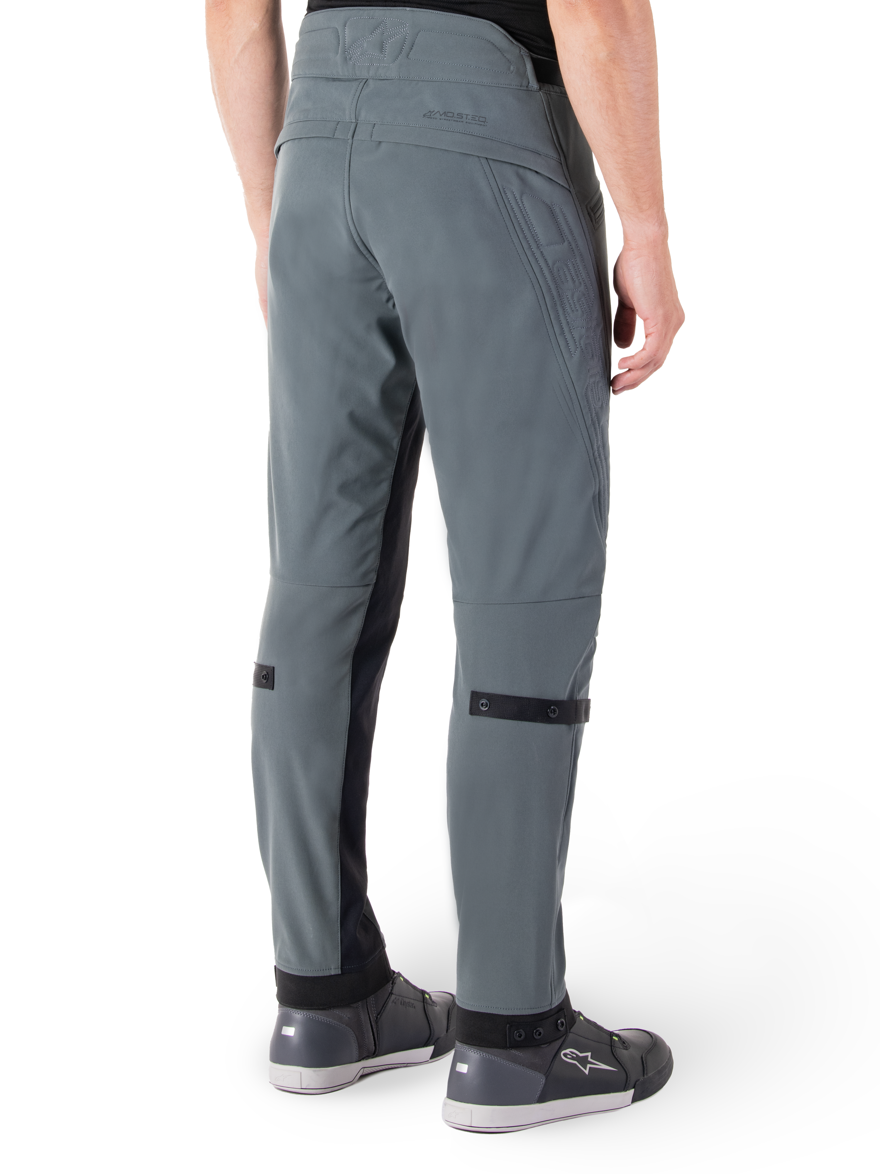 Pantalones Alpinestars Alden, Gris Urbano, vista lateral trasera, pantalones técnicos de conducción inspirados en el estilo urbano con detalles acolchados en la cintura y correas negras en la pantorrilla, combinados con calzado de conducción gris, equipamiento de motociclismo urbano moderno