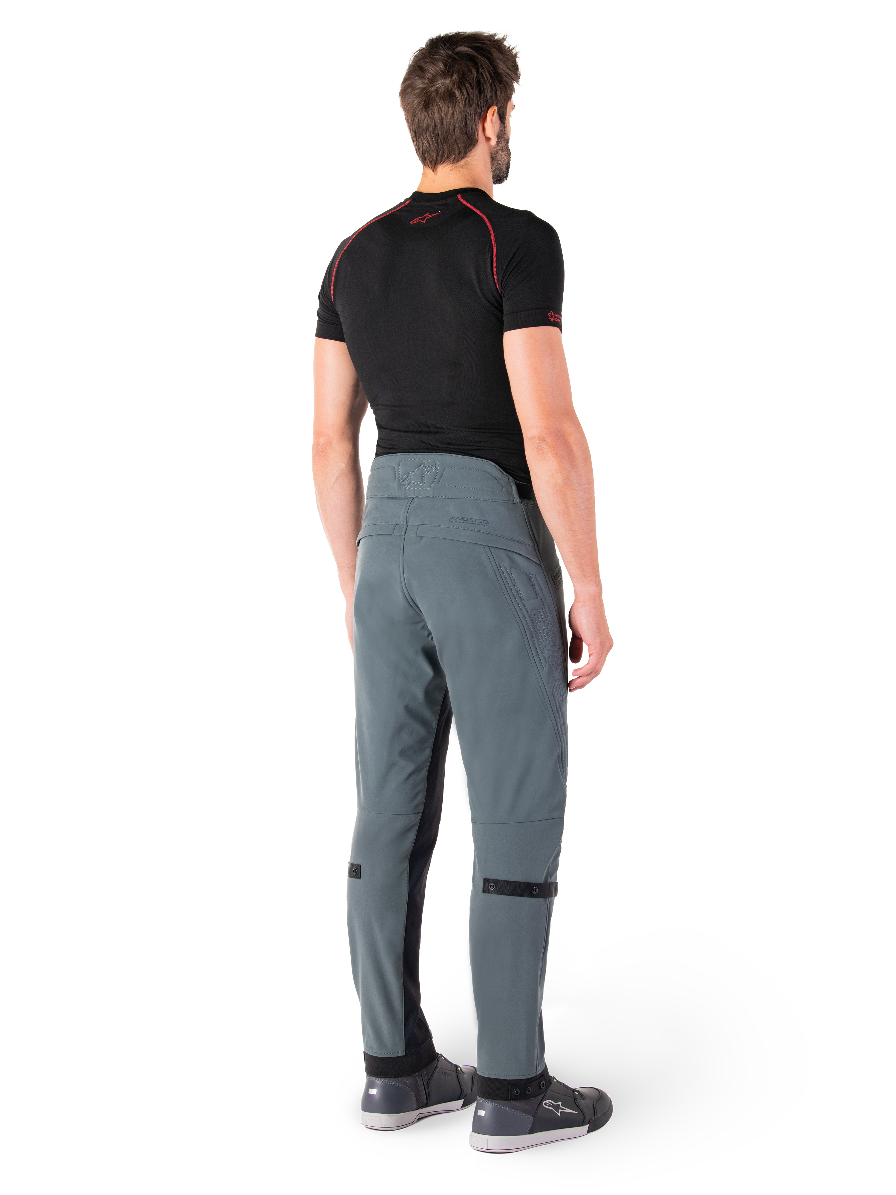 Pantalones Alpinestars Alden, Urban Gray, vista trasera, pantalones de moto de tejido técnico con detalles acolchados en la parte superior trasera de la cintura y las piernas, combinados con una capa base negra y calzado de conducción gris, estilo streetwear urbano contemporáneo.