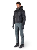 Pantalones Alpinestars Alden en Urban Gray, llevados por un modelo con una chaqueta negra acolchada con capucha, guantes y calzado de conducción, con detalles acolchados en los laterales y paneles interiores negros en las piernas, equipamiento urbano para moto inspirado en el estilo streetwear.