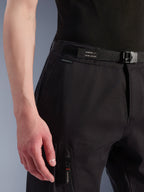Alpinestars Flex-AST Cargo Pants, color negro, primer plano de la zona de la cintura y la cadera, con cinturón ajustable integrado con marca Alpinestars, cierre de hebilla y un bolsillo cargo con cremallera, tejido elástico técnico para equipamiento de moto urbano